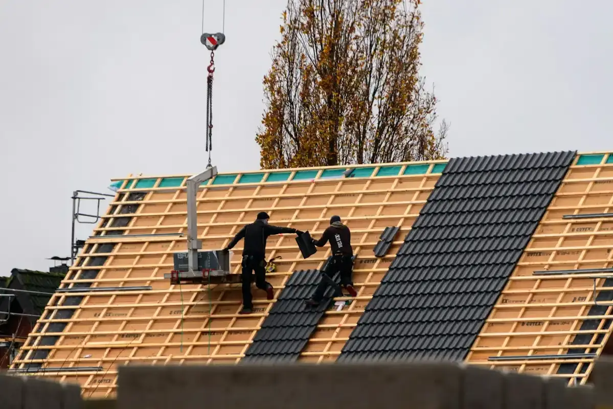 Zwei Dachdecker decken ein Steildach mit dunklen Dachziegeln neu ein