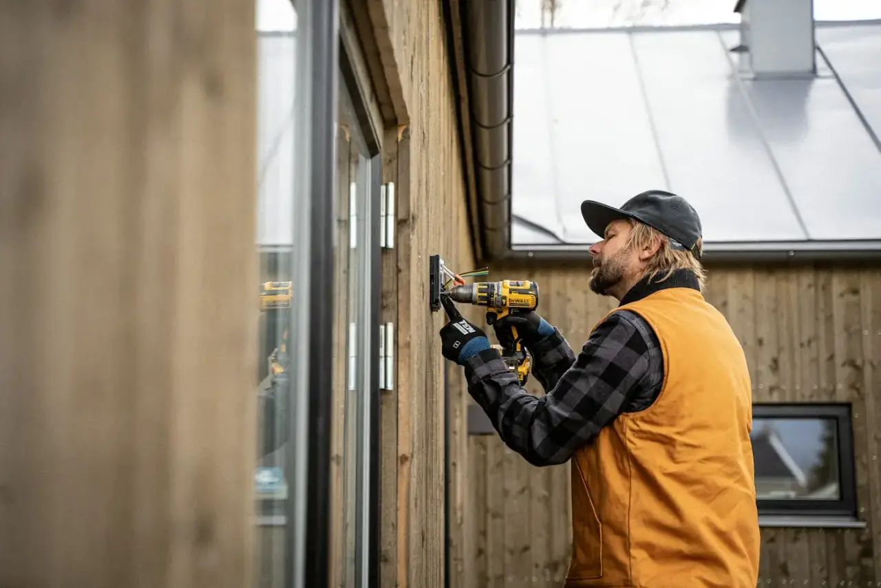 Handwerker arbeitet mit dem Akkubohrer an einer Holzfassade