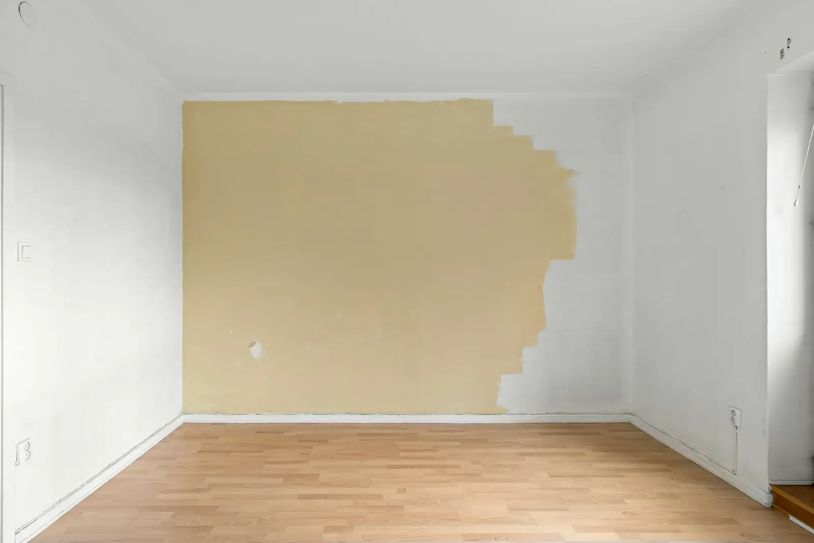 Leeres Zimmer, eine Wand ist zur Hälfte neu in Beige gestrichen